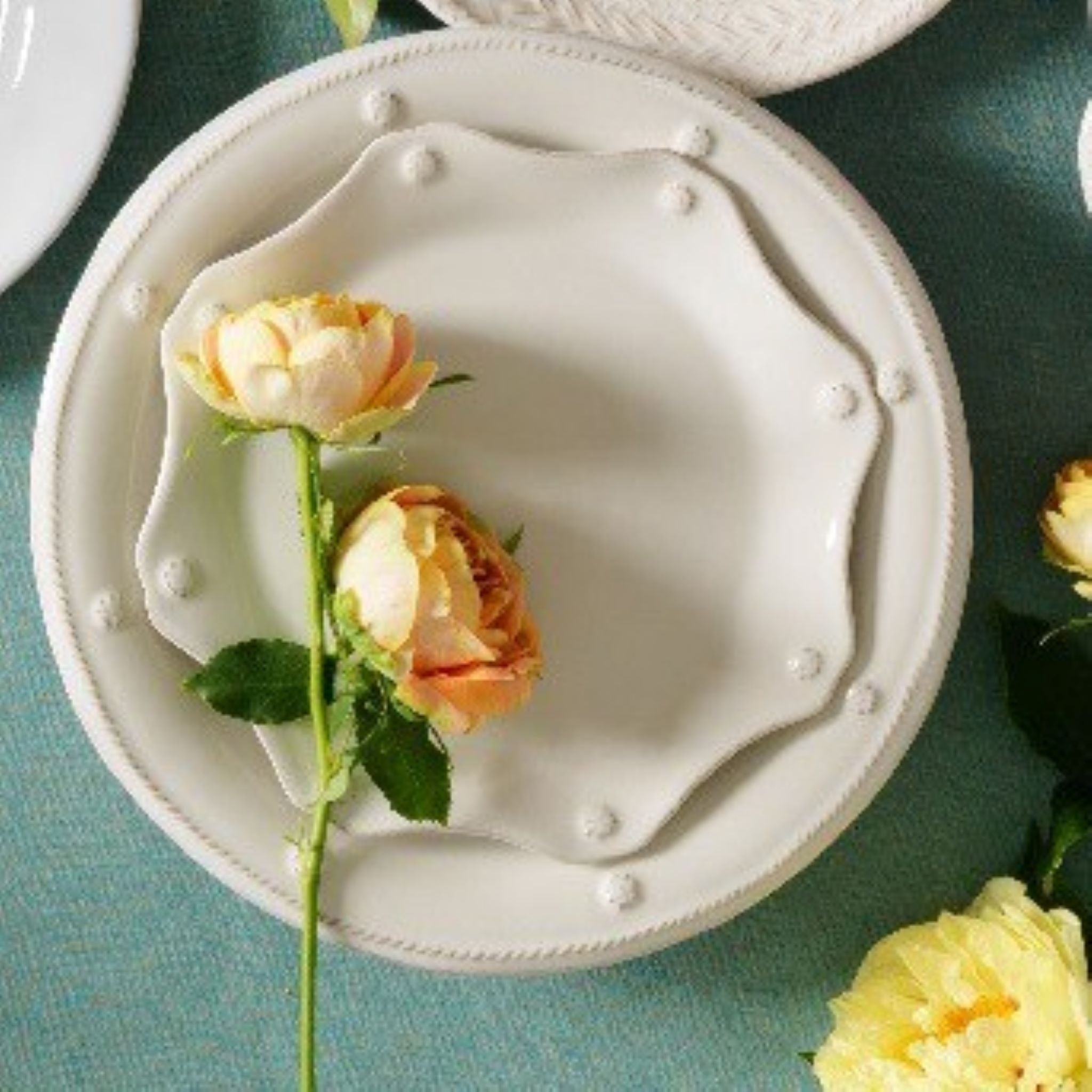 A stem of ranunculus sits atop Juliska's Berry & Thread scalloped salad plate which sits atop a Berry & Thread dinner plate.