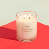 A lit two-wick Glasshouse Fragrances' candle sits on a red table. 