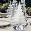 A collection of Simon Pearce glass tabletop evergreens (fronted by the Snowdrift Evergreen) sit lined up on a table.