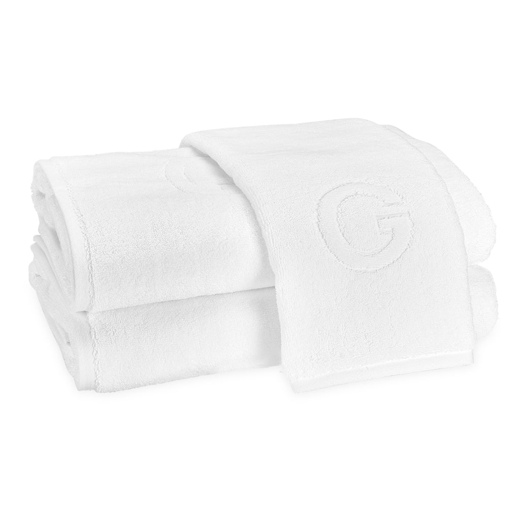A stack of two bath towels and one hand towel laid on top with the block letter "G" initial.
