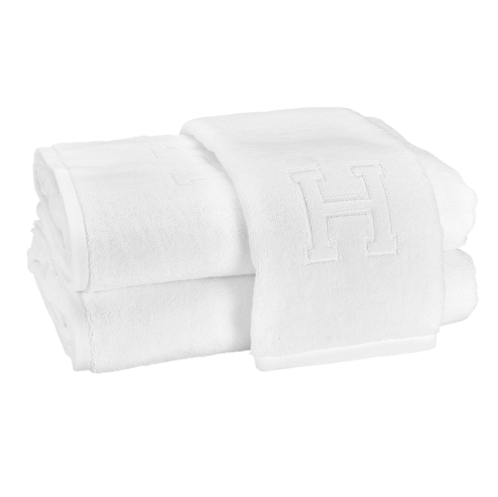 A stack of two bath towels and one hand towel laid on top with the block letter "H" initial.