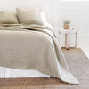 A bed made up with Pom Pom at Home's Huntington diamond-patterned coverlet in taupe over white sheets and bedskirt. 