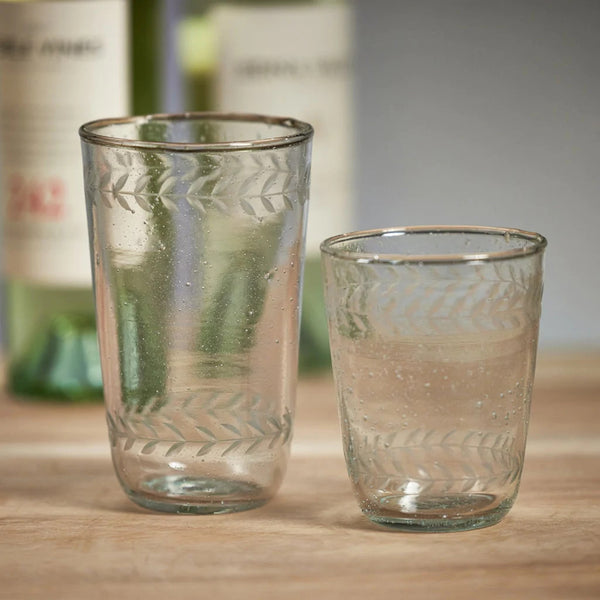 Glassware from the Colette collection features bubbles blown into the glass and vitage etching around the top and bottom rims. In this photo, there is a tall tumbler and a small tumbler.