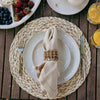 A table set for breakfast with plates and cutlery on a woven placemat. A linen napkin is cinched with a Juliska Provence woven rattan napkin ring.