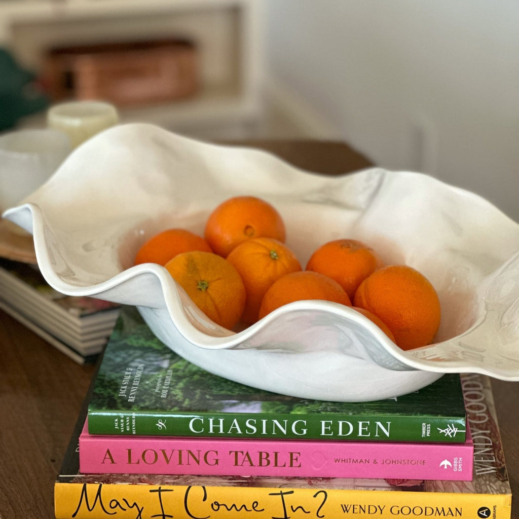 Cream wavy melamine bowl full of oranges, stacked on three books on a table. 