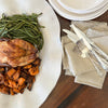 White wavy platter with a turkey and green beans, next to a stack of plates and silverware on a wood table.