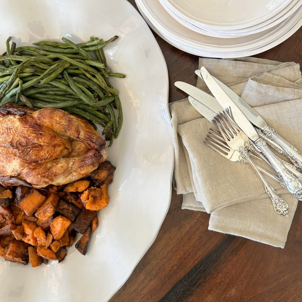 White wavy platter with a turkey and green beans, next to a stack of plates and silverware on a wood table.