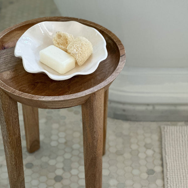 Cream wavy melamine bowl filled with soap and sponges on a small round table.