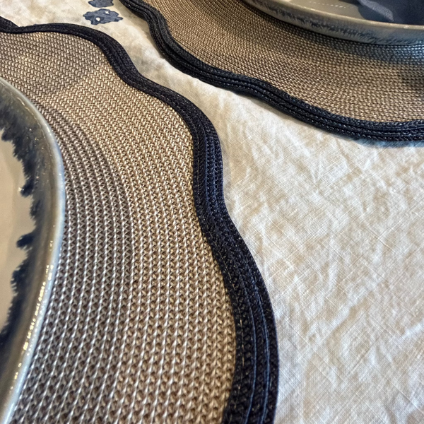 Close up image of navy and bone braided placemat with scalloped edge on cream tablecloth.