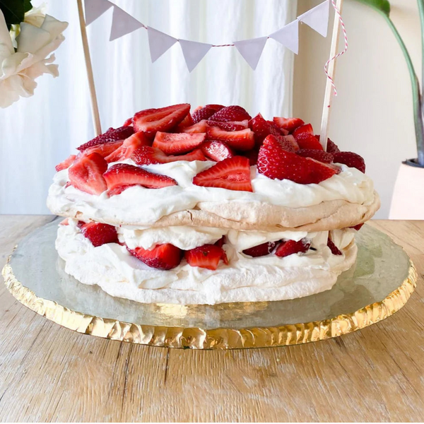 Strawberry cake on a gold rimmed cake stand with decorative flags in the background.