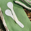 Two small mother of pearl spoons on a green linen napkin and rattan charger. 