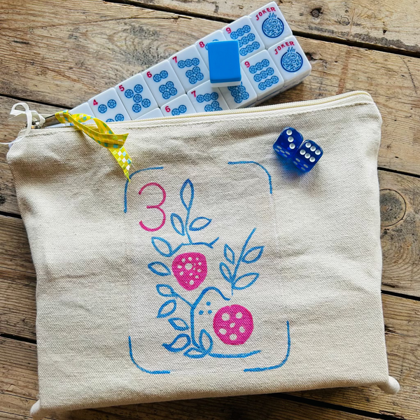 Fabric pouch with hand painted design, dice, and mahjong tiles on a wooden surface