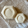 Two bars of soap with honeycomb pattern and beehive imprint on tan hand towel. 