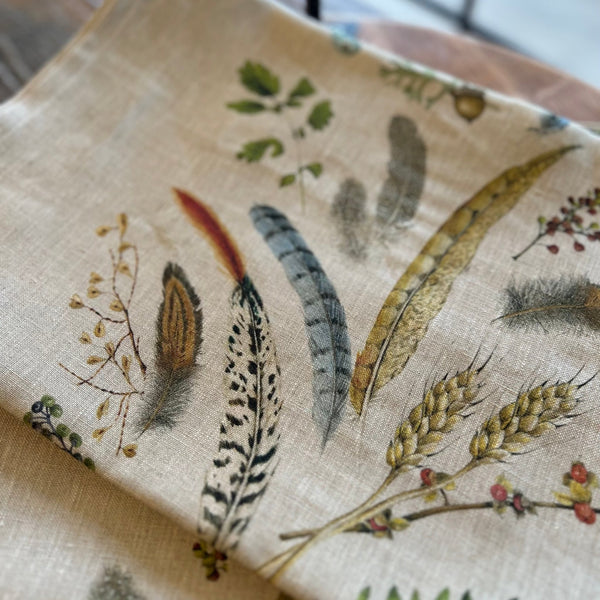 Natural linen table runner with renderings of feathers, leaves, eggs, acorns and other natural objects. 