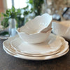 Scalloped, melamine plates and bowls stacked on metal table in front of green flowers in glass vases. 