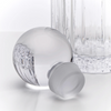 A clear glass bottle with a frosted screw cap lying on its side, with a ribbed clear glass bottle body standing behind it on a white studio background.