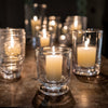 Group of cylindrical hurricane candle holders on dark wood table with dark background.