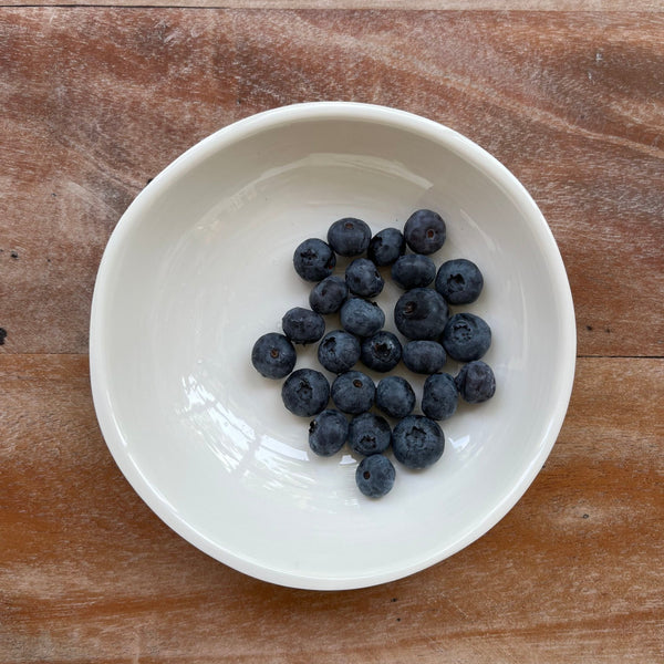 Blueberries in cream bowl on wooden table.