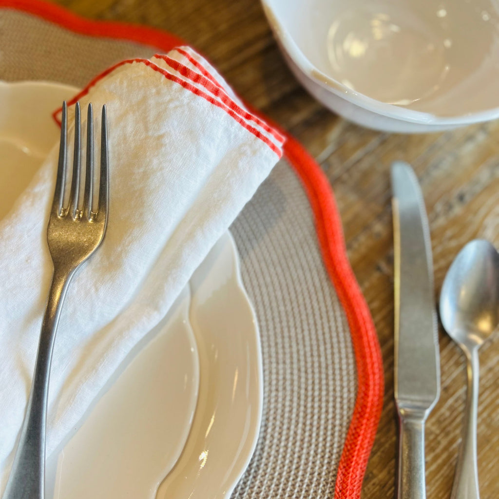 Place setting with linen napkin with coral trim on wooden table. 