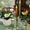 A grouping of three green bobbin shaped candlesticks with lit green candles sits on a set dinner table.