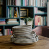 Stone, melamine plates and bowls stacked on a wooden table.