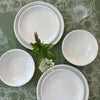 White bowls and plates on green table cloth with small vase and flowers.