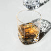 Simon Pearce Woodbury Whiskey Glass with brown liguqe and shadow on white background.