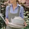 Woman in grey apron carrying melamine dishes in the garden. 