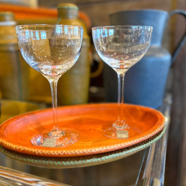 Two Nick and Nora Simon Pearce glasses on an orange leather tray with green and blue leather barware accessories in the background. 