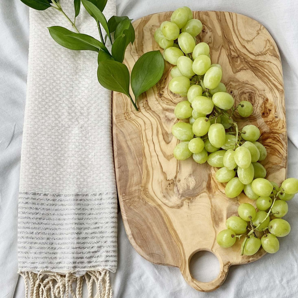 Olivewood cheeseboard with grapes on a cream tablecloth with cream handtowel. 