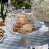 Decorative glass cake stand with pastries on a table setting with flowers and glasses.