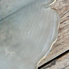 Edge of frosted glass scalloped platter with gold edge on wooden table.