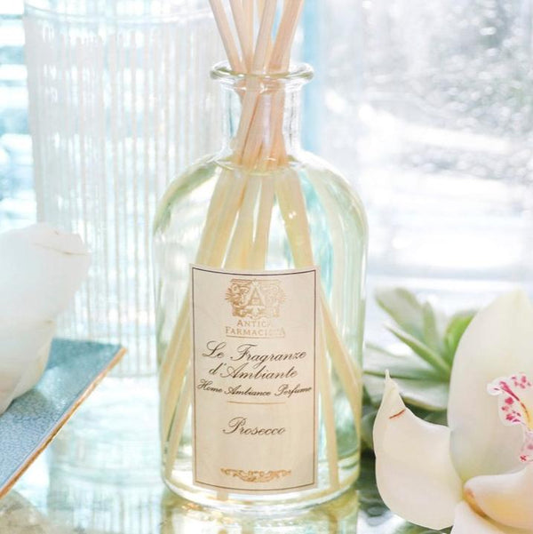 Reed diffuser on a glass surface with flower in foreground.