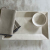 Cream rectangle tray with linen napkins and small bowl on marble counter.