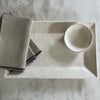 Cream rectangle tray with small bowl and linen napkins on white marble counter.