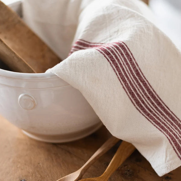 White ceramic bowl with wooden spoons and a striped towel on a wooden surface