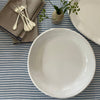 Double Line Cream bowl and platter on striped table cloth with linen napkin, forks and vase with green flowers. 