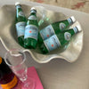 Wavy melamine bowl with water bottles next to pink book on an ottoman.