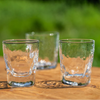 Three Simon Pearce Woodbury Whiskey glasses on a wooden surface with a blurred green background