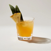 Simon Pearce Woodbury Double Old Fashion Glass with orange juice and a pineapple wedge on a light gray background