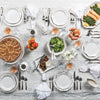 Overhead view of table set with Juliska Berry & Thread dinnerware, bakeware, silverware, napkins and glasses. Platters and bowls hold salmon, salad and a dessert tart.