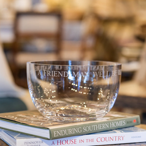 Clear glass 8.5 inch diameter bowl with engraved sentiment around the rim:  "A friend may well be reckoned the masterpiece of nature." The bowl is placed upon a stack of books.