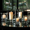 Various clear glass Simon Pearce candleholders grouped on a table. It is evening and there are lit candles placed inside.