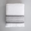 One Mungo white waffle weave bath towel, folded. Two thick and two thin gray stripes are woven near the fringed edge.