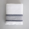 One Mungo white waffle weave bath towel, folded. Two thick and two thin blue stripes are woven near the fringed edge.