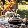Simon Pearce Ascutney glass wine decanter filled with red wine sits on a table with fall decorattions. 