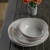 Stack of Relish melamine double lined plates and bowls on a talbe decorated with a flower vase.
