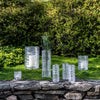 Seven Simon Pearce Echo Lake clear glass vases of varying sizes sit outside on a mossy patch atop a stone wall.