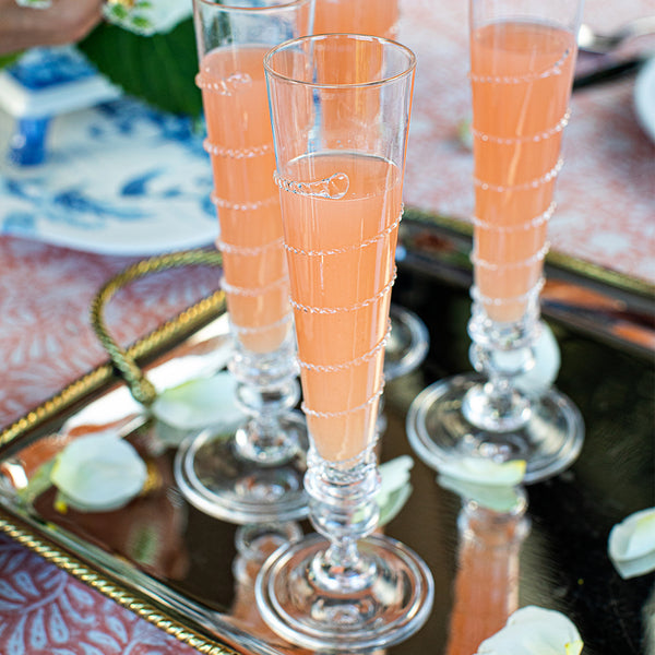 Four Juliska Amalia flutes filled with pink juice and sitting on a shiny tray atop a table.