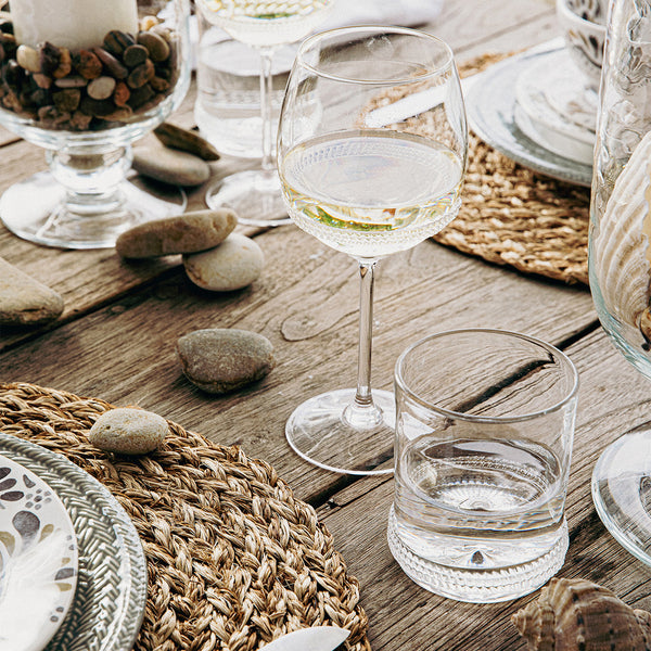 Juliska Dean stemmed wine glass and double old fashioned glass on a table set with placemats, dinnerware, and candles.